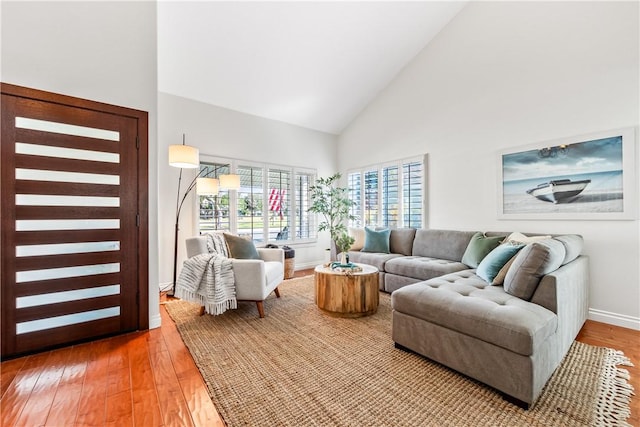 living room featuring high vaulted ceiling, baseboards, and light wood finished floors