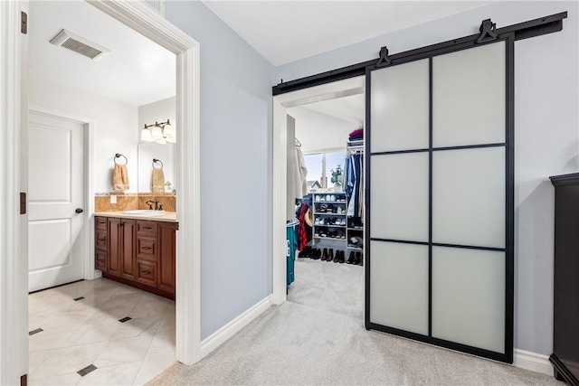 hall with visible vents, a sink, light carpet, and a barn door