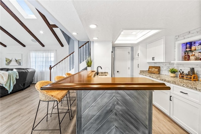 bar with tasteful backsplash, a skylight, beam ceiling, and light wood finished floors