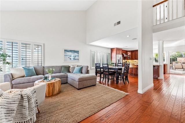 living room featuring a towering ceiling, a wealth of natural light, visible vents, and wood finished floors