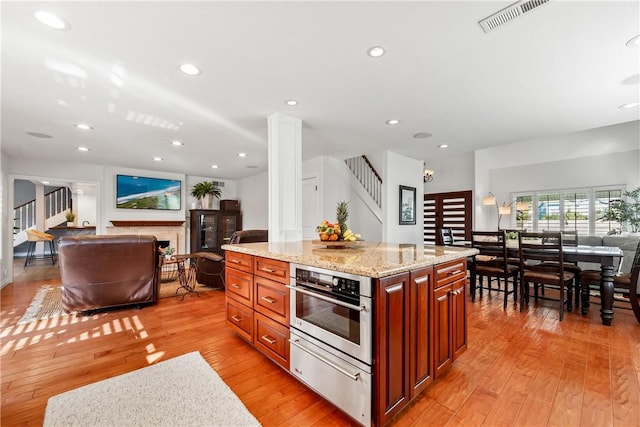 kitchen featuring a warming drawer, a fireplace, visible vents, open floor plan, and stainless steel oven