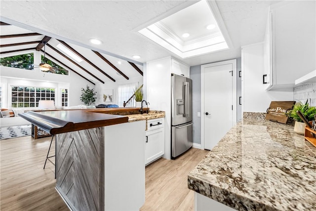 kitchen featuring a skylight, light wood-style flooring, beamed ceiling, white cabinetry, and high end fridge