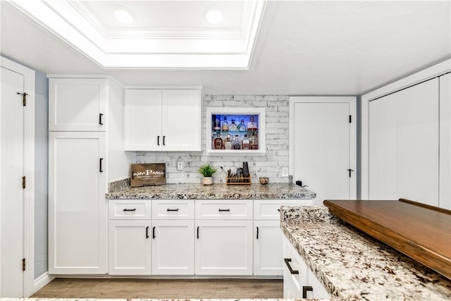 bar featuring a bar, ornamental molding, a raised ceiling, and backsplash