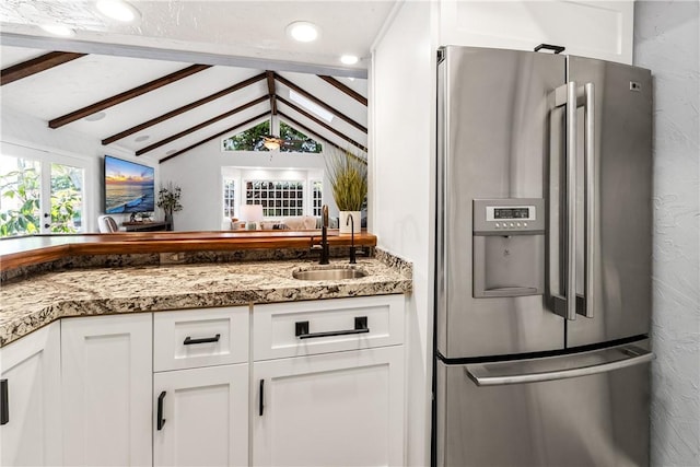 kitchen with stone countertops, white cabinets, stainless steel fridge with ice dispenser, vaulted ceiling with beams, and a sink