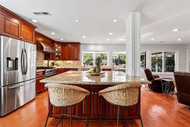 kitchen featuring wall chimney exhaust hood, light stone counters, stainless steel appliances, and light wood-style flooring