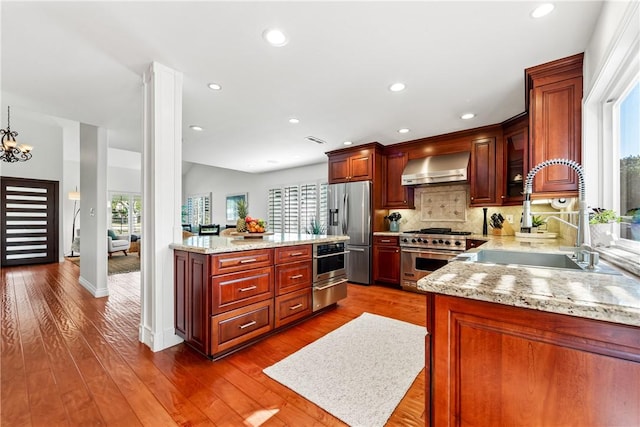 kitchen with dark wood-style flooring, a sink, appliances with stainless steel finishes, decorative backsplash, and wall chimney exhaust hood