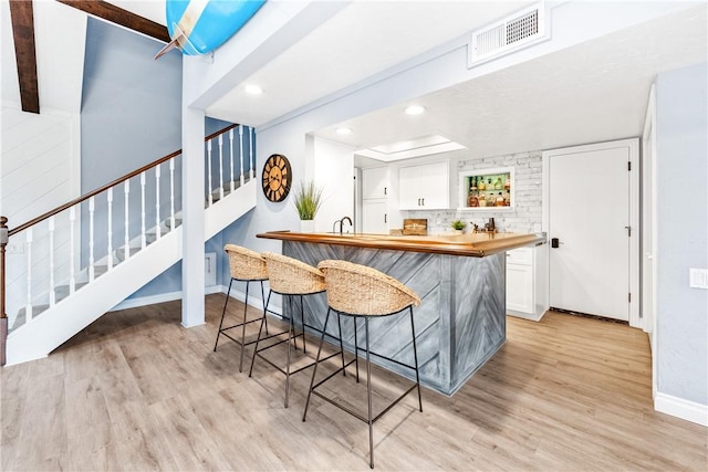 bar featuring stairs, baseboards, visible vents, and light wood-style floors