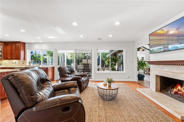 living area with baseboards, recessed lighting, a tile fireplace, and light wood-style floors