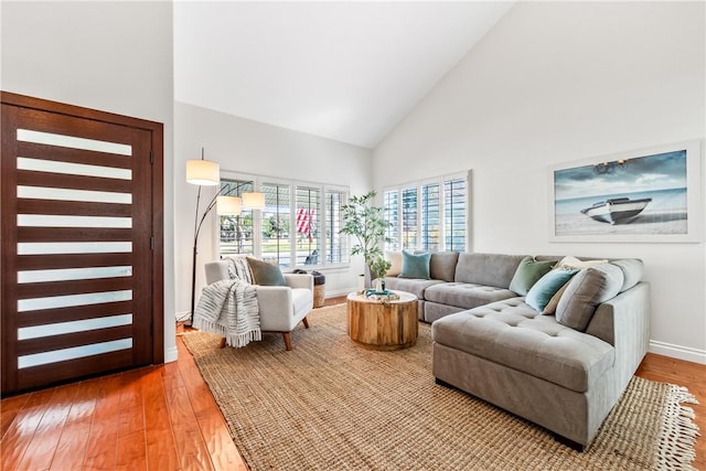 living area featuring baseboards, high vaulted ceiling, and light wood-style floors