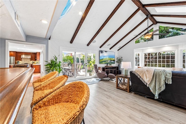 living area featuring a skylight, a ceiling fan, french doors, light wood-type flooring, and beam ceiling