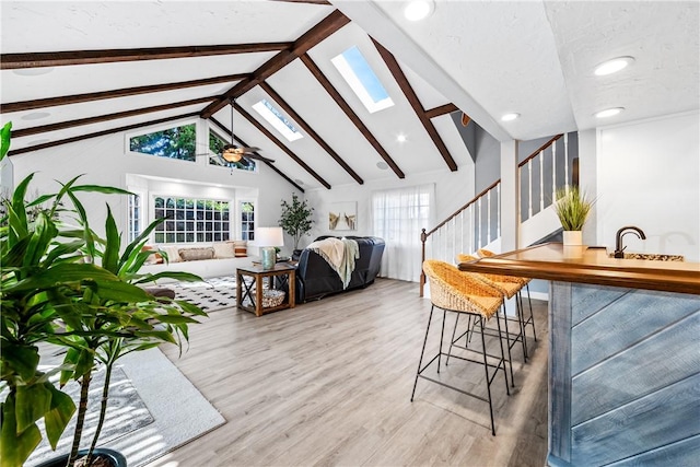 living room featuring a skylight, beam ceiling, stairway, and wood finished floors