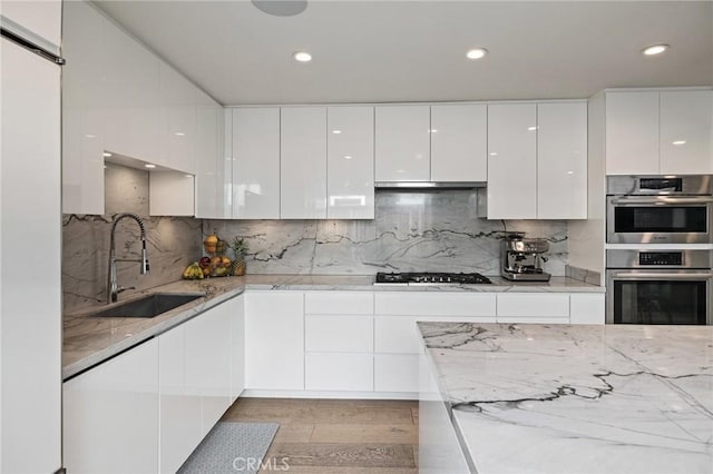 kitchen with sink, appliances with stainless steel finishes, white cabinetry, light stone counters, and tasteful backsplash