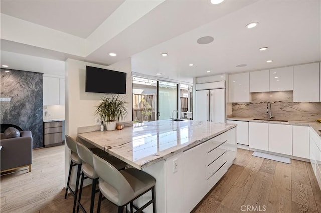 kitchen featuring a breakfast bar, tasteful backsplash, white cabinets, light stone counters, and paneled fridge