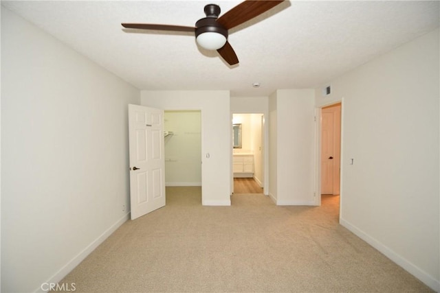 unfurnished bedroom featuring ceiling fan, a spacious closet, a closet, and light carpet