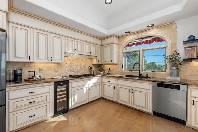 kitchen with sink, stainless steel appliances, cream cabinets, a raised ceiling, and beverage cooler