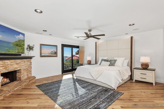 bedroom with ceiling fan, a stone fireplace, access to outside, and light wood-type flooring