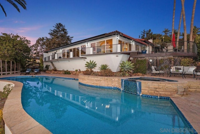 pool at dusk featuring a patio area and an in ground hot tub