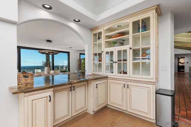 bar featuring cream cabinets, pendant lighting, dark stone countertops, and light hardwood / wood-style flooring