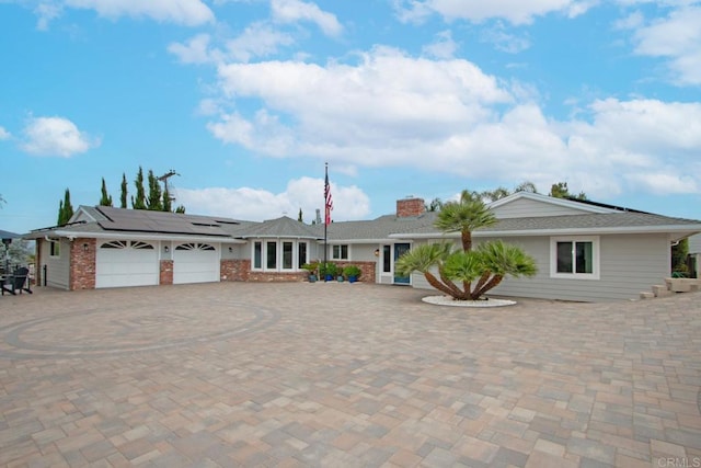 ranch-style home with roof mounted solar panels, an attached garage, a chimney, and decorative driveway