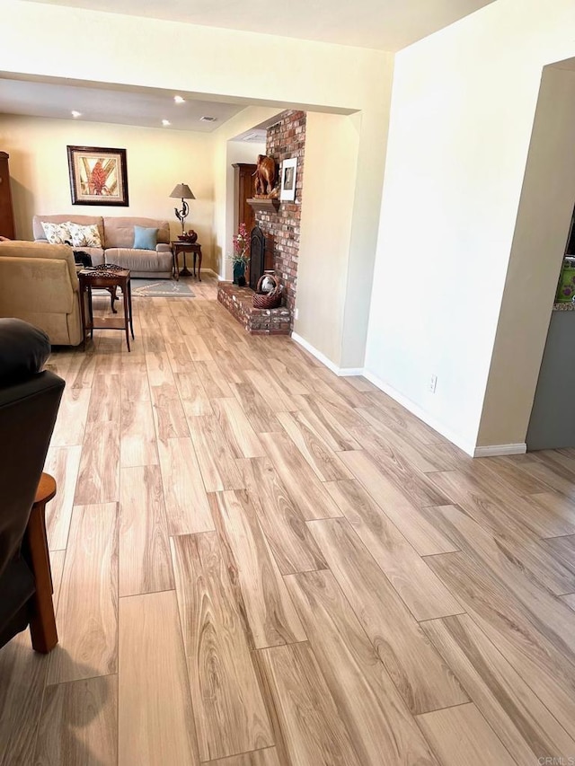 living room featuring a brick fireplace, light wood-style floors, and baseboards