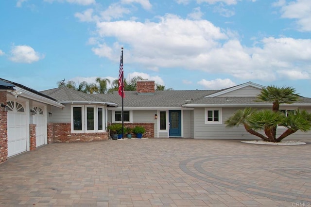 view of front of house featuring decorative driveway, brick siding, and a chimney