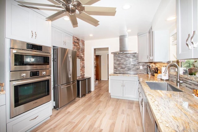 kitchen with light wood finished floors, backsplash, ventilation hood, appliances with stainless steel finishes, and a sink