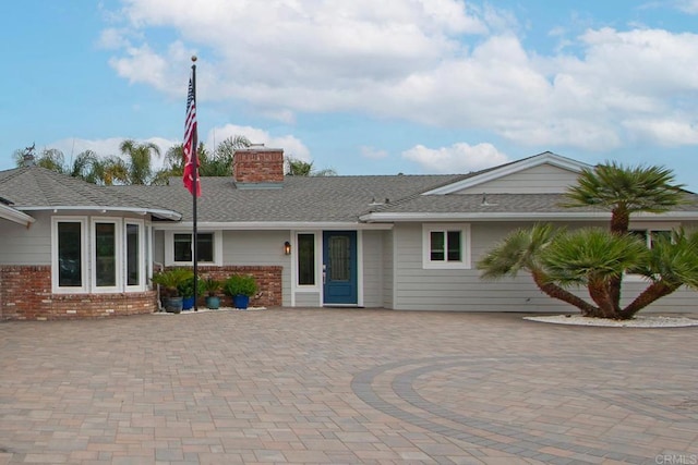 view of front of home with brick siding, roof with shingles, and a chimney