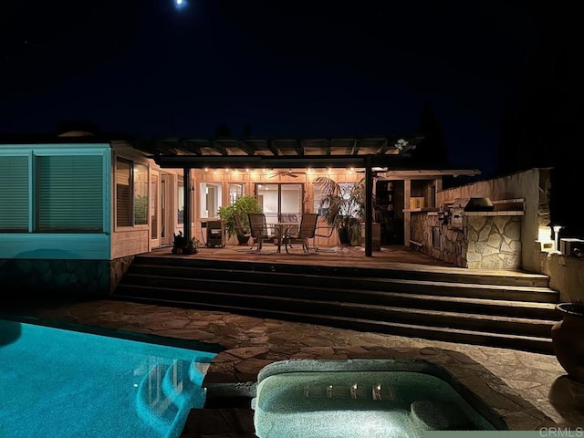 back of house at twilight with outdoor dining space, an in ground hot tub, exterior kitchen, and a deck