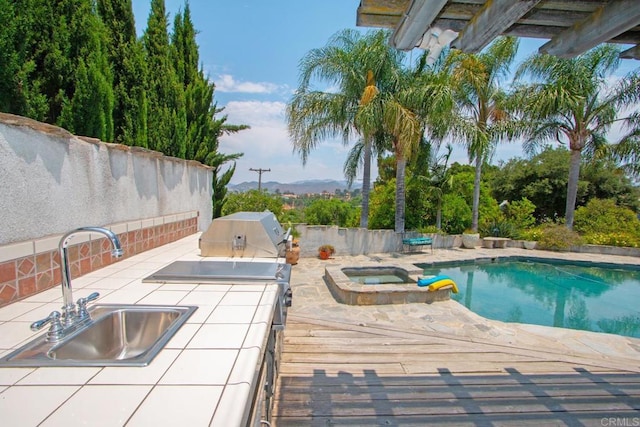 view of pool featuring a pool with connected hot tub, a sink, grilling area, exterior kitchen, and a patio area