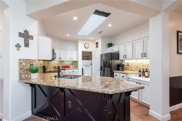 kitchen featuring sink, white cabinets, washer / clothes dryer, black refrigerator with ice dispenser, and kitchen peninsula