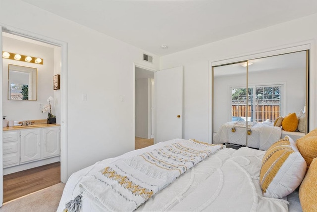 bedroom featuring light colored carpet, connected bathroom, sink, and a closet