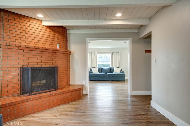 unfurnished living room with beam ceiling, a brick fireplace, and light wood-type flooring