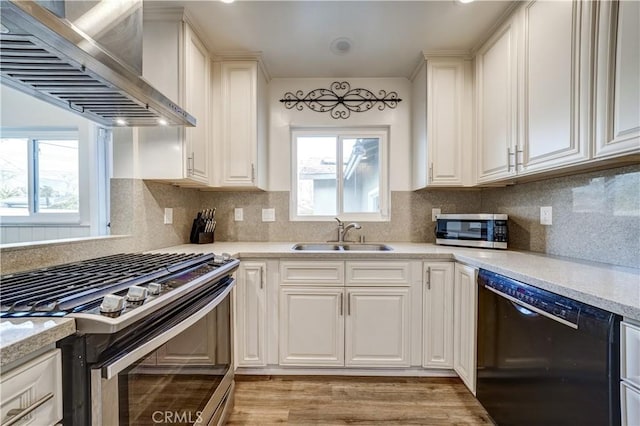 kitchen with appliances with stainless steel finishes, tasteful backsplash, sink, white cabinets, and wall chimney exhaust hood