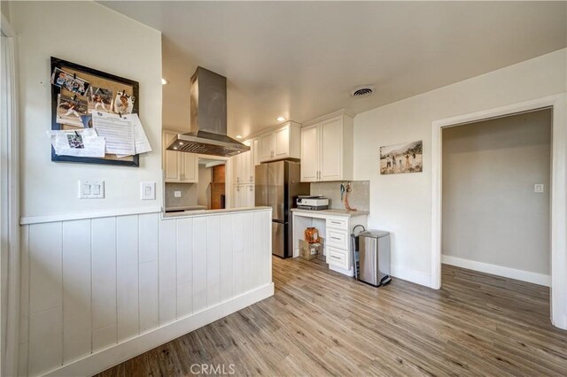 kitchen featuring stainless steel refrigerator, white cabinetry, island range hood, and light hardwood / wood-style floors