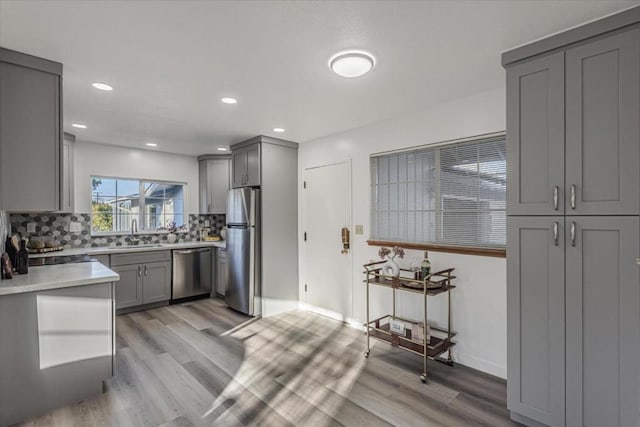 kitchen with tasteful backsplash, appliances with stainless steel finishes, gray cabinets, and light hardwood / wood-style flooring