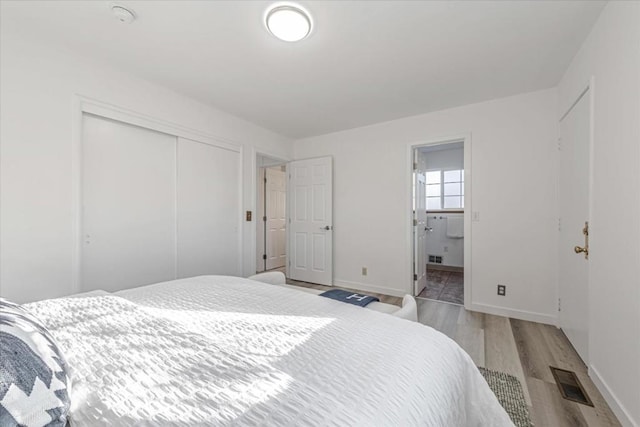 bedroom featuring a closet, ensuite bath, and light hardwood / wood-style flooring