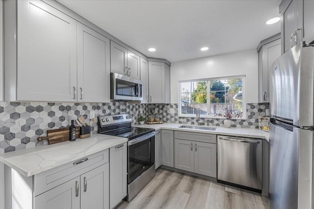 kitchen with sink, gray cabinets, appliances with stainless steel finishes, light stone countertops, and light hardwood / wood-style floors