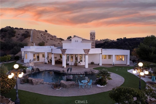 back house at dusk featuring a mountain view and a patio area