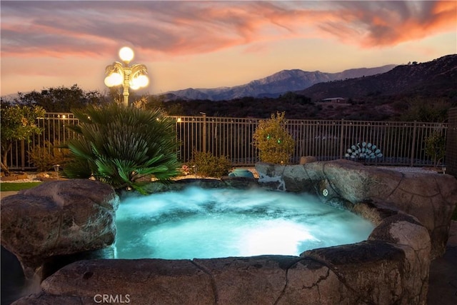 pool at dusk with a mountain view and a hot tub