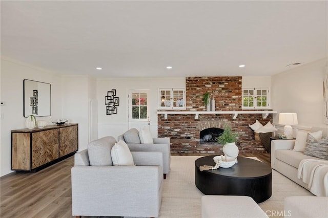 living room featuring a brick fireplace, ornamental molding, and light hardwood / wood-style floors