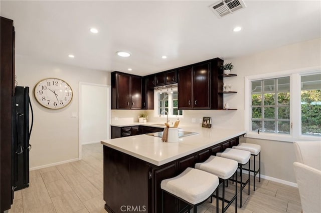 kitchen with black electric cooktop, dark brown cabinets, a kitchen breakfast bar, and kitchen peninsula