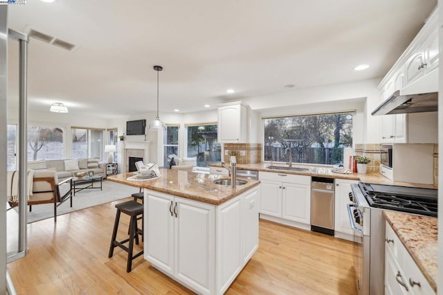 kitchen with sink, white cabinets, light stone counters, stainless steel gas range oven, and a center island with sink