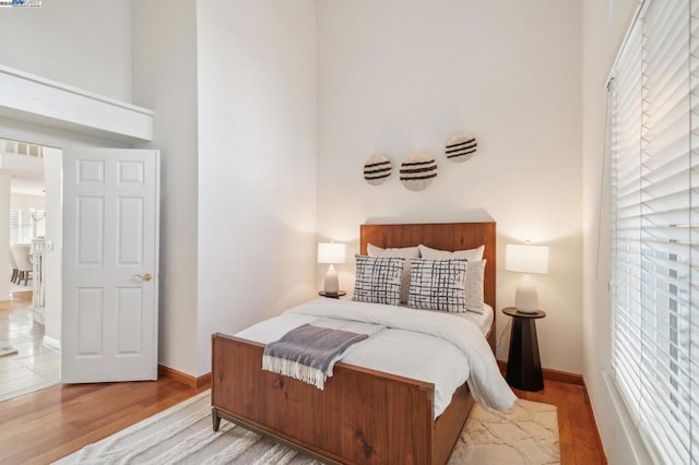 bedroom with multiple windows, light hardwood / wood-style floors, and a high ceiling