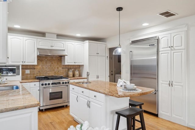 kitchen with built in appliances, sink, decorative light fixtures, and white cabinetry