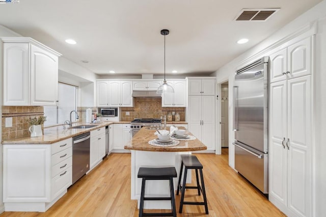 kitchen featuring sink, high end appliances, white cabinetry, a center island, and hanging light fixtures