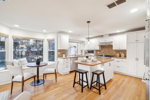 kitchen featuring sink, white cabinetry, a center island, hanging light fixtures, and appliances with stainless steel finishes