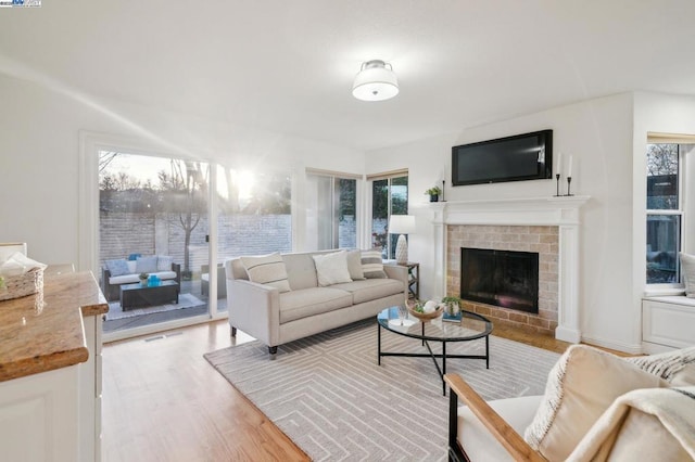 living room featuring a brick fireplace, light hardwood / wood-style flooring, and a healthy amount of sunlight