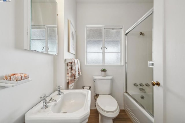 bathroom with hardwood / wood-style flooring, enclosed tub / shower combo, and toilet