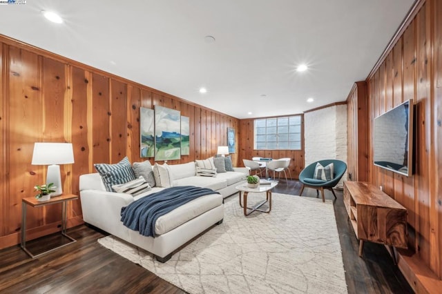 living room featuring dark wood-type flooring, ornamental molding, and wood walls