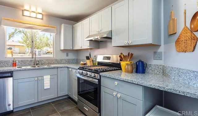 kitchen with appliances with stainless steel finishes, white cabinetry, sink, dark tile patterned floors, and light stone countertops